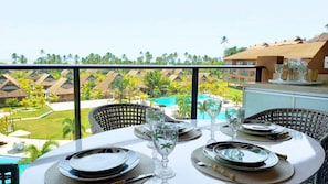 A dining area with a table set for four, overlooking a pool and resort buildings. - Lindos apartamentos no Eco Resort (Tamandaré)
