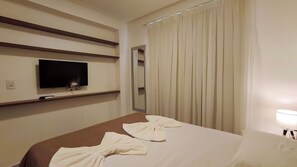 A hotel room with a bed, a TV mounted on the wall, a mirror, and a window with curtains. - Lindos apartamentos no Eco Resort (Tamandaré)