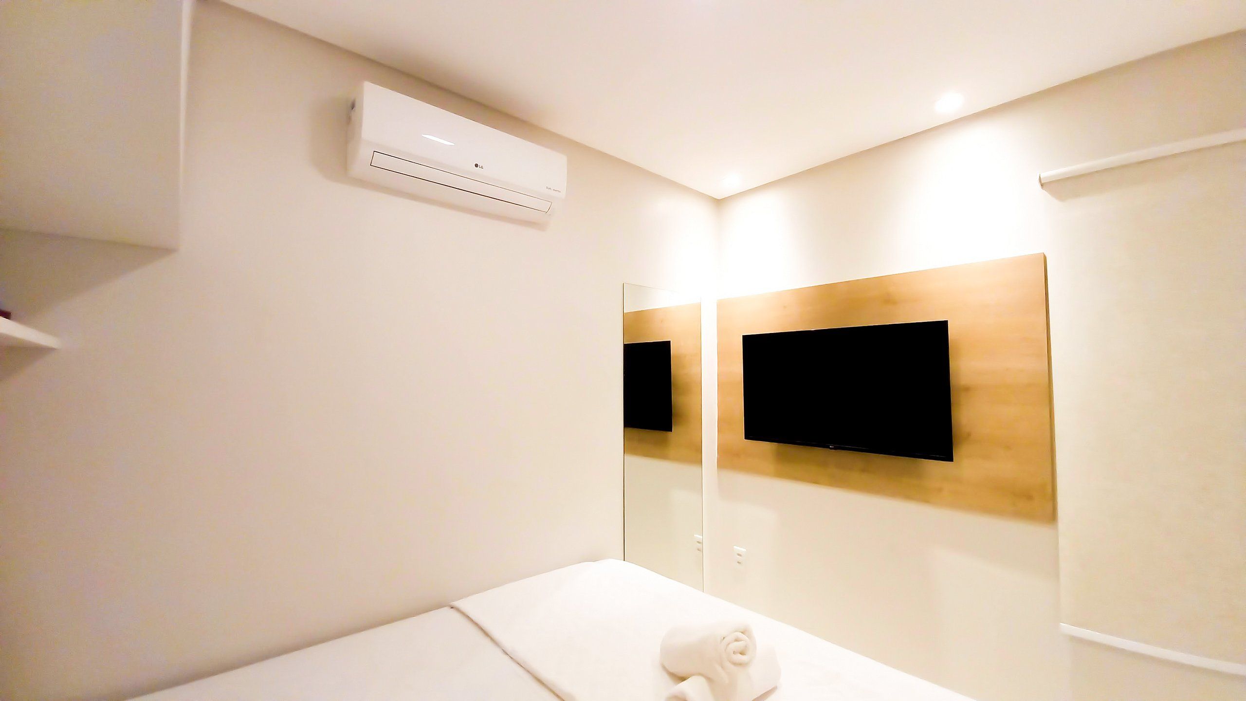 Ein Hotelzimmer mit einem Bett, einem flachbildfernseher an einer Holzvertäfelung, einer wandmontierten Klimaanlage und einem Handtuch auf dem Bett.