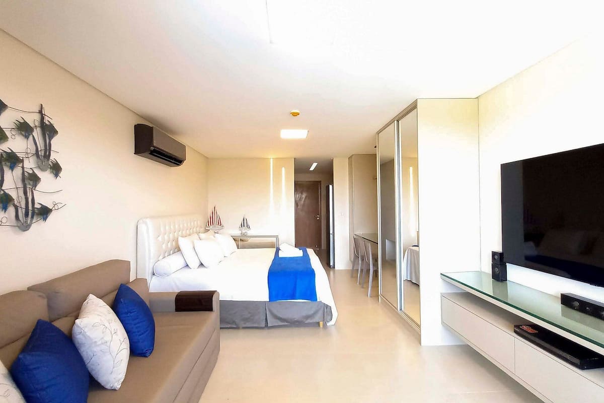 A hotel room with a bed, a sofa, a TV, and a wall-mounted artwork.