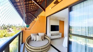 Un balcon avec un canapé en osier, un téléviseur fixé au mur et une porte vitrée donnant sur une pièce.