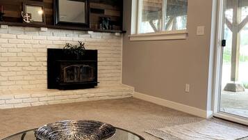 A living room with a white brick fireplace, a glass coffee table, and a view through a glass door.