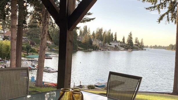 A glass table with chairs and a view of a lake with boats and houses in the background. - Lakefront Apartment on Beautiful Lake Tapps, Spectacular Views (Bonney Lake)