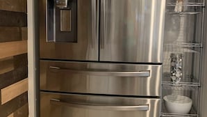 A stainless steel refrigerator with a water dispenser and a built-in ice maker, a wire shelf with jars and a bowl, and a wooden wall panel. - Lakefront Apartment on Beautiful Lake Tapps, Spectacular Views (Bonney Lake)
