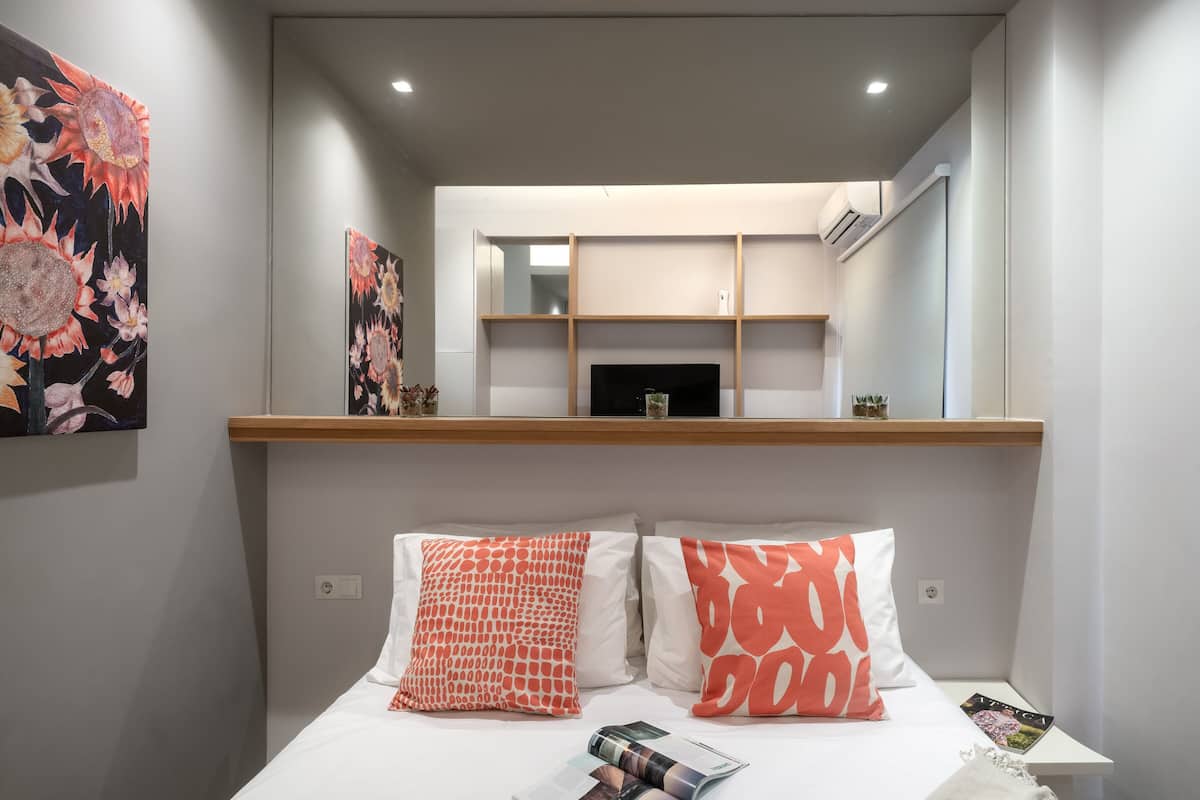 A bedroom with a bed, two pillows, a magazine, and a mirror above the bed.