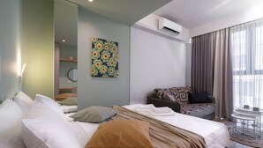 A modern hotel room with a bed, a sofa, a small table, and a large window with curtains. - Kolokotroni Lofts Syntagma (Athens)