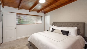 Un dormitorio con techo de madera, una cama con ropa de cama blanca y una ventana con persianas.