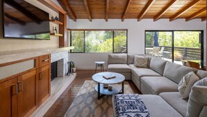 Una sala de estar moderna con chimenea, techo de madera, ventanas amplias y una zona de estar acogedora.