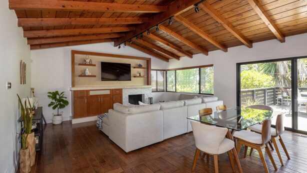 Una cocina moderna con una isla grande, vigas de techo de madera y una mesa de comedor de vidrio con sillas.