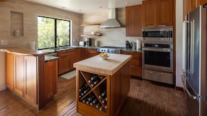 Cocina moderna con armarios de madera, electrodomésticos de acero inoxidable y una estantería para vinos.
