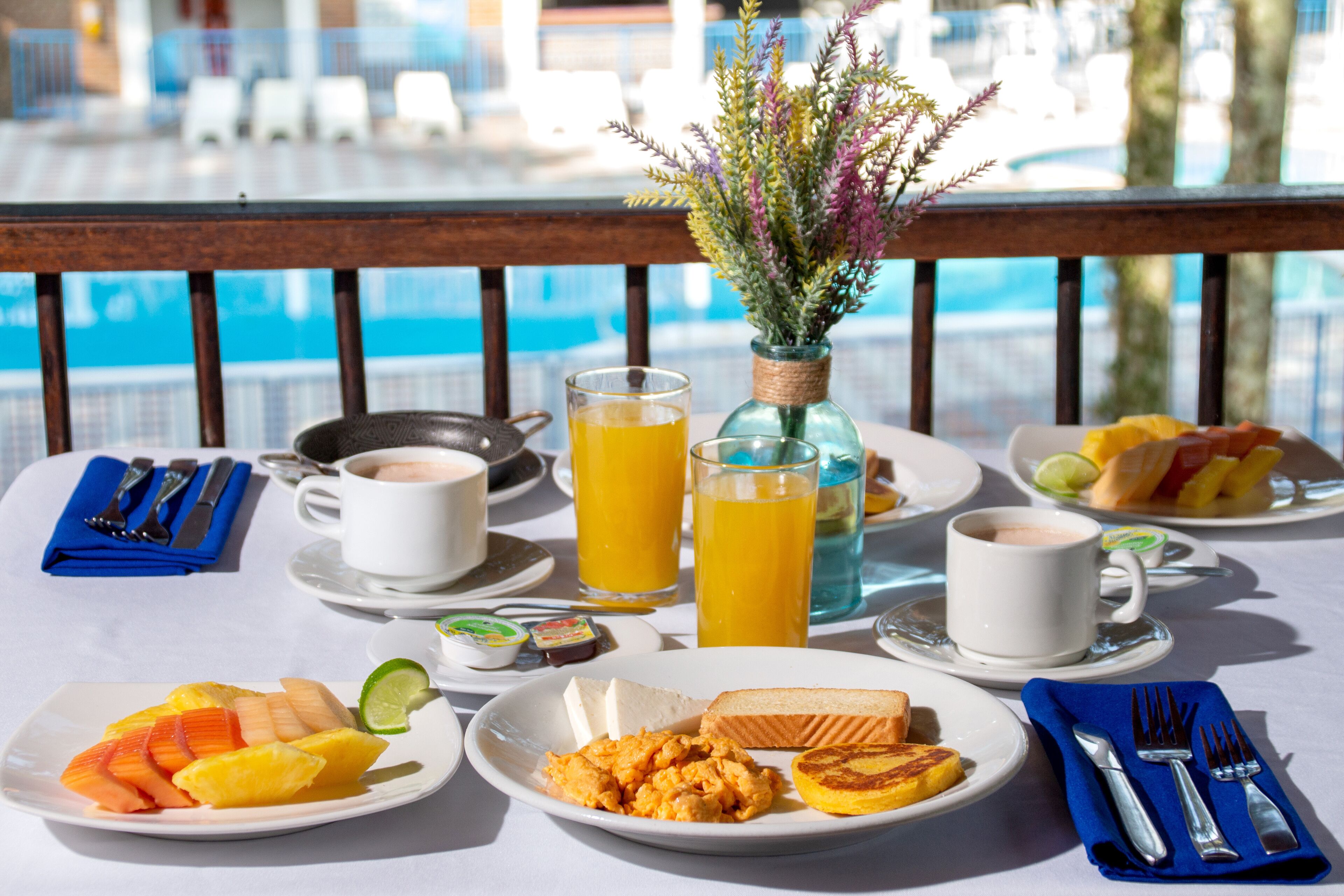 A breakfast table with plates of food, drinks, and a vase of flowers.