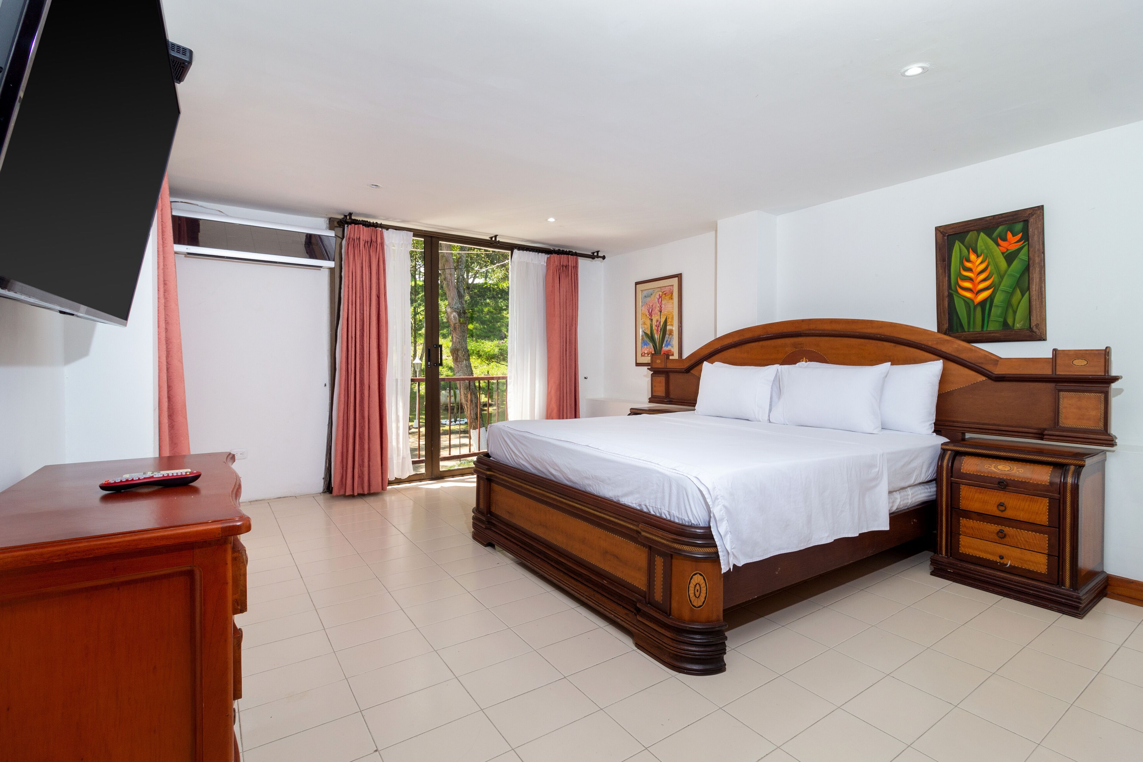 A bedroom with a large bed, wooden nightstands, a TV, and a sliding glass door to the outside.