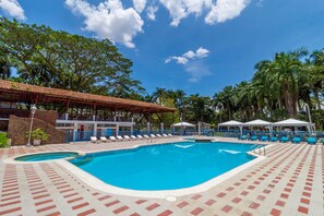 Una piscina con cubierta de baldosas, sillas de descanso y sombrillas.