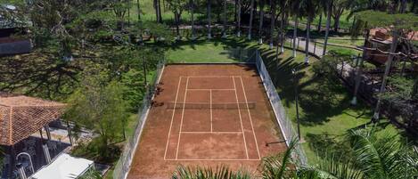 Cancha de tennis a l'aire lliure envoltada de vegetació abundant i palmeres.