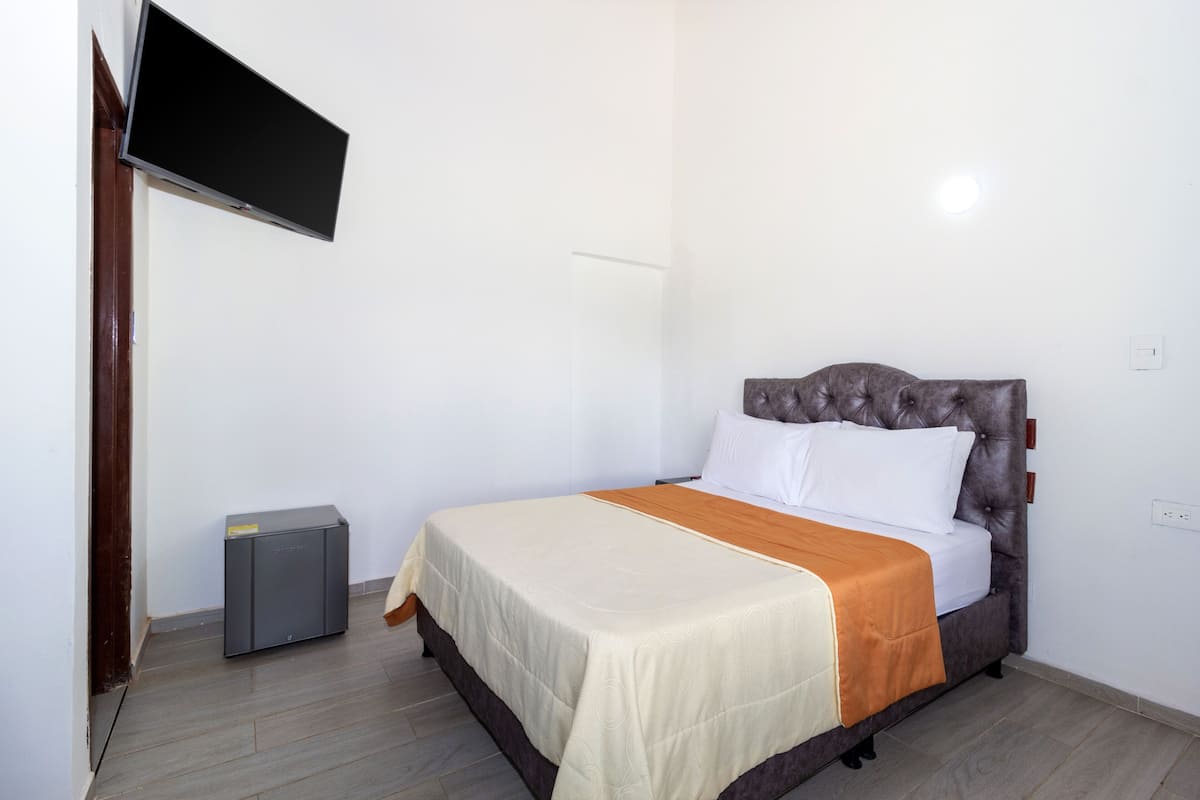 A neatly made bed with a headboard, a bedside table, and a flat-screen TV mounted on the wall.