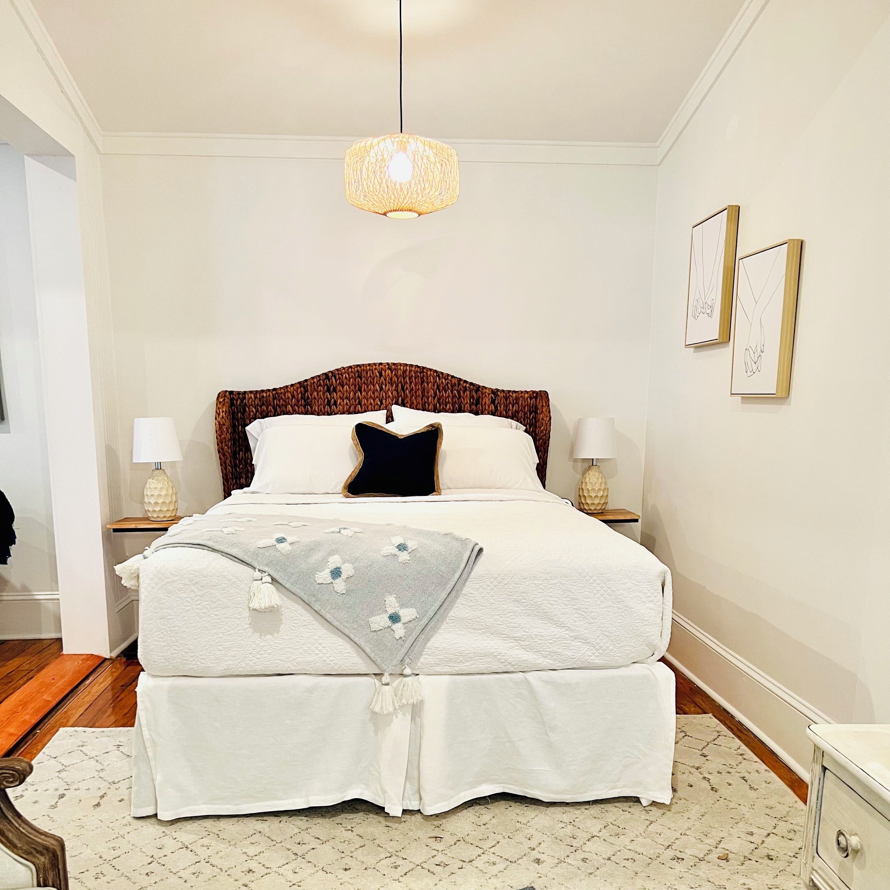 A neatly arranged bedroom with a large bed, two bedside lamps, a hanging light fixture, and framed artwork on the wall.