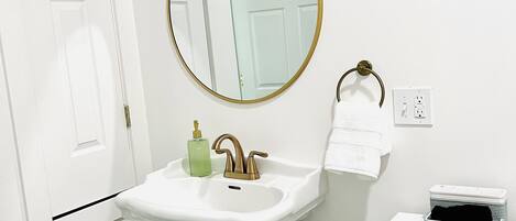 Un baño con un lavabo blanco, un espejo con marco dorado, un inodoro blanco y una cesta debajo del lavabo.
