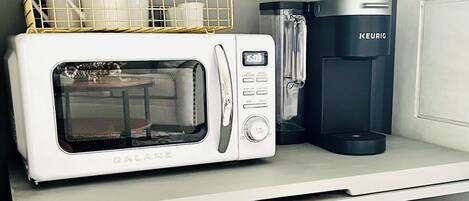 Une petite cuisine équipée d’un micro-ondes blanc, d’une machine à café noire et d’une cafetière en verre.
