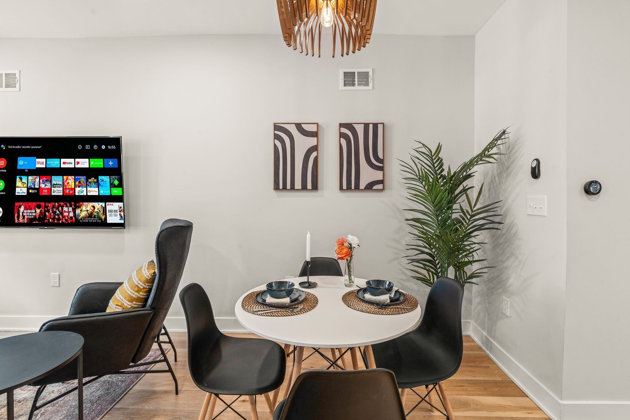 A modern dining area with a round table, black chairs, and a mounted TV displaying a streaming service interface.