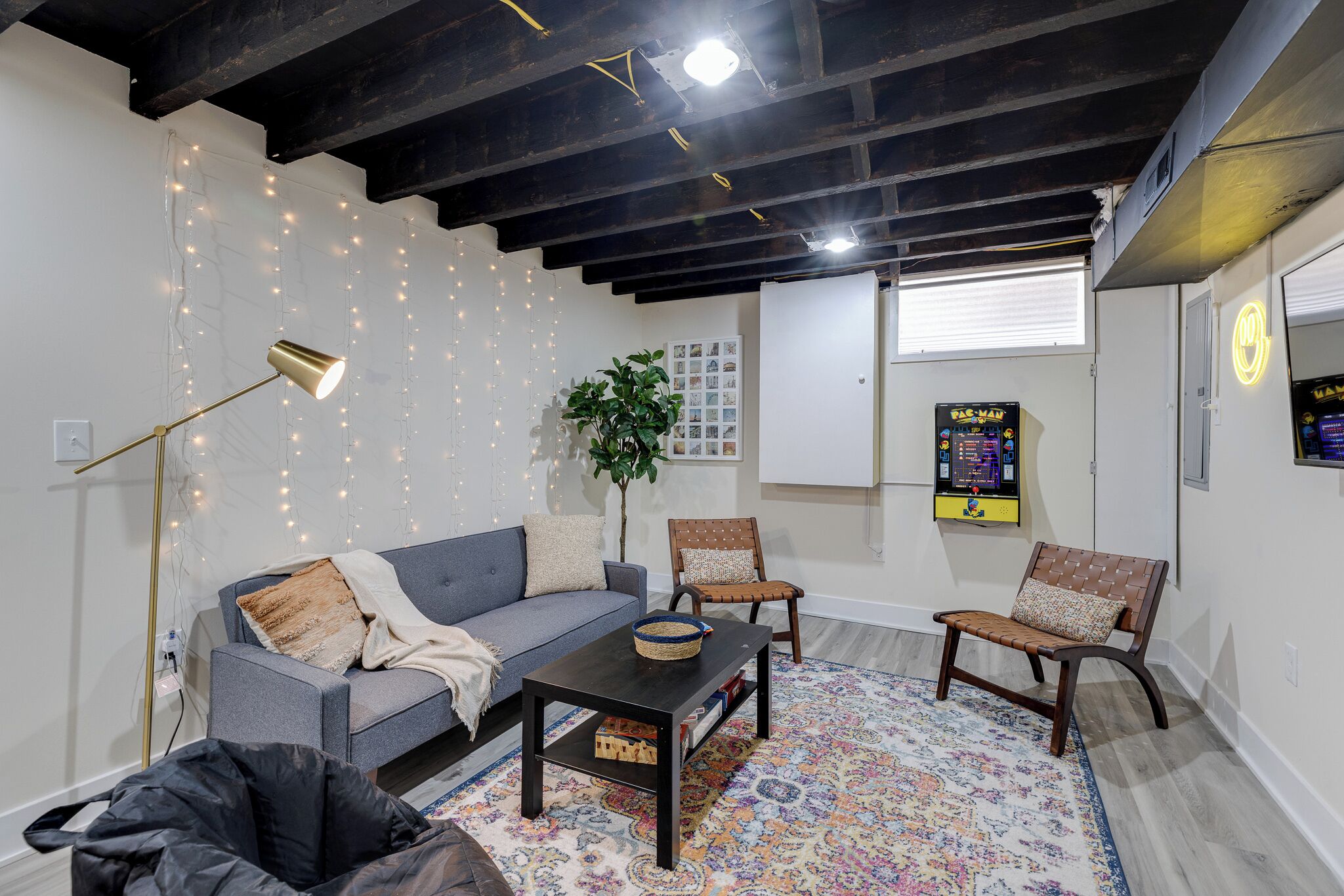 Ein Wohnzimmer mit grauem Sofa, zwei Holzstühlen, einem Couchtisch, einer Stehlampe und einem gemusterten Teppich.