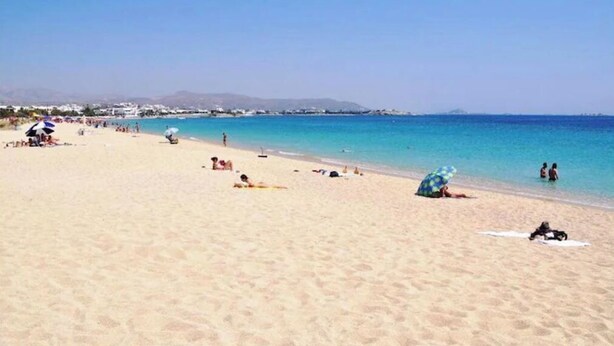 A beach with people sunbathing and swimming, clear blue water, and a distant mountain range. - Spacious 2BR Flat, Pergola Veranda, 20m to Agios Prokopios Beach (Naxos)