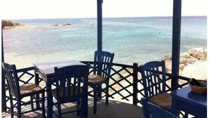 A seaside terrace with blue chairs and a table, overlooking the ocean. - Spacious 2BR Flat, Pergola Veranda, 20m to Agios Prokopios Beach (Naxos)