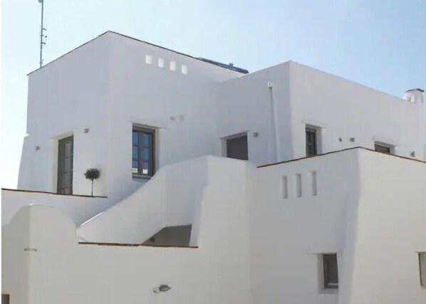 A modern white building with a flat roof, multiple windows, and a small balcony.
