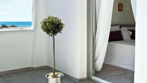 A balcony with a potted plant, a bed with white bedding, and a view of the sea. - Spacious 2BR Flat, Pergola Veranda, 20m to Agios Prokopios Beach (Naxos)