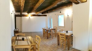 Un espace repas avec des tables et des chaises en bois, un sol en briques et des poutres apparentes en bois au plafond.