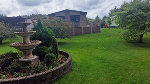 Un jardín con una fuente de piedra, una terraza de madera y un edificio al fondo.