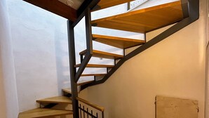 A spiral staircase with wooden steps and black metal railings in a room with white walls and a wooden floor.