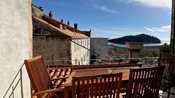 Une terrasse avec une table et des chaises, donnant sur une zone côtière avec des bâtiments et une colline.