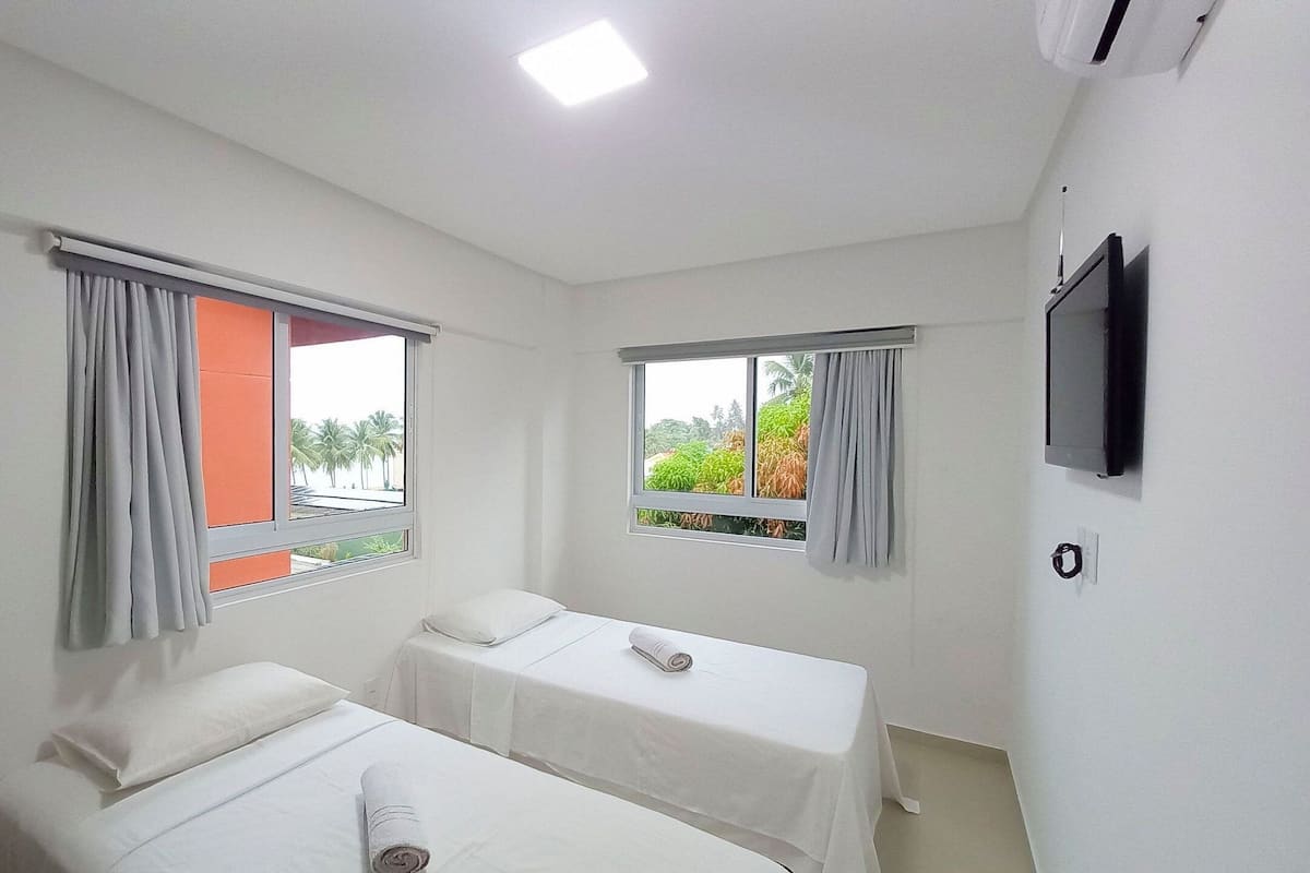 Una habitación de hotel con dos camas individuales, un televisor montado en la pared y ventanas con cortinas.