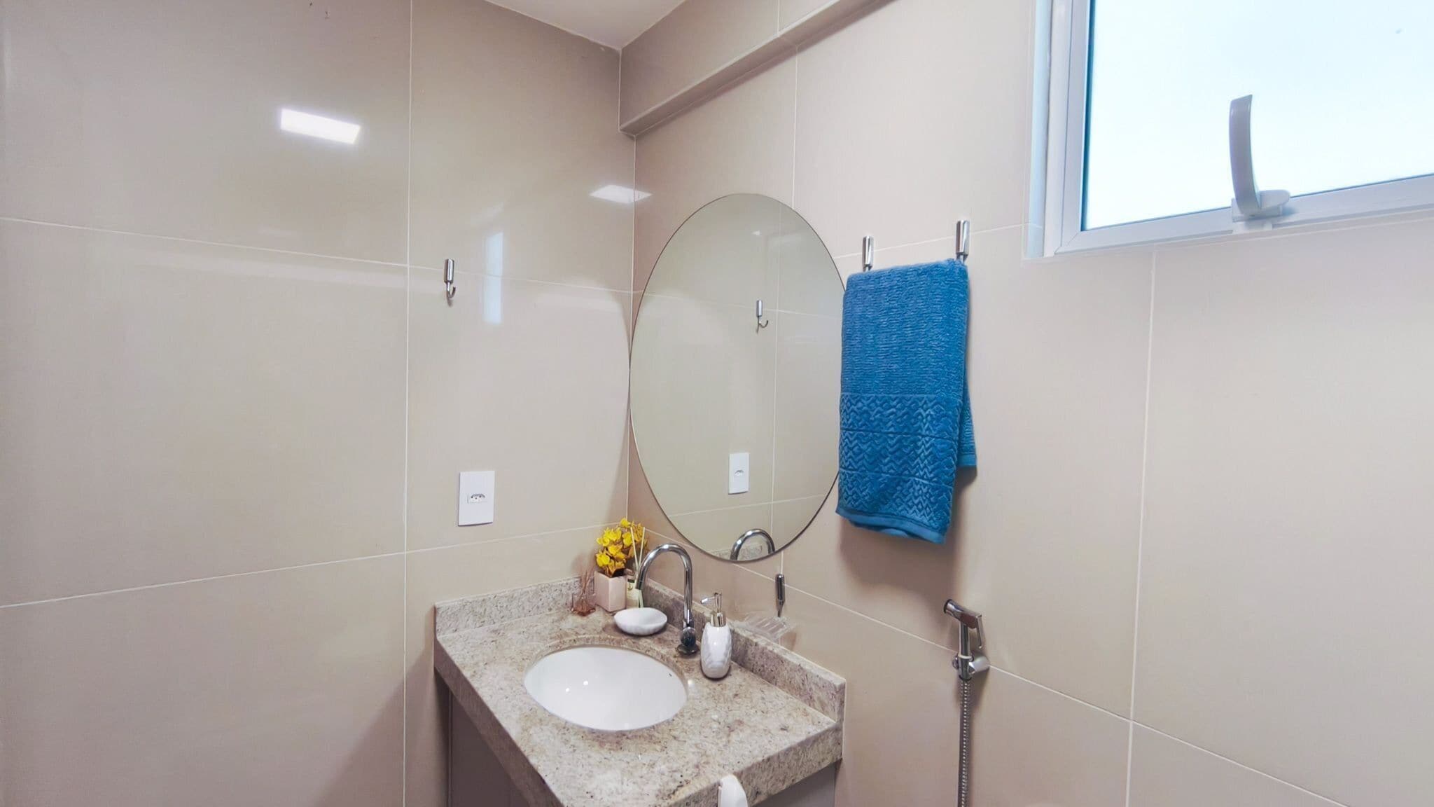 Un baño con un espejo redondo, un lavamanos, un perchero para toallas y una ventana.