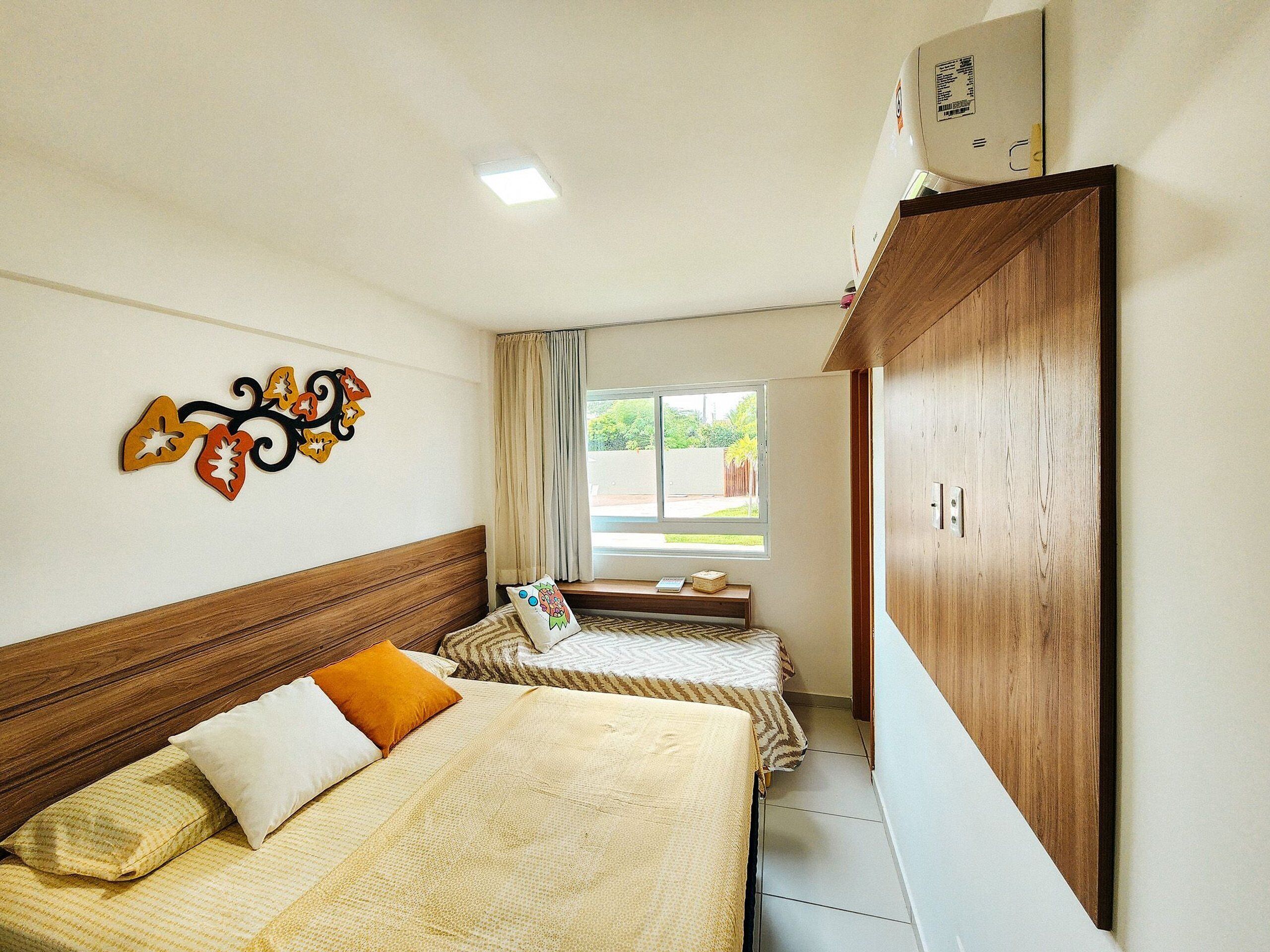 A hotel room with two beds, a wooden headboard, a decorative wall piece, a window with curtains, and a wardrobe.