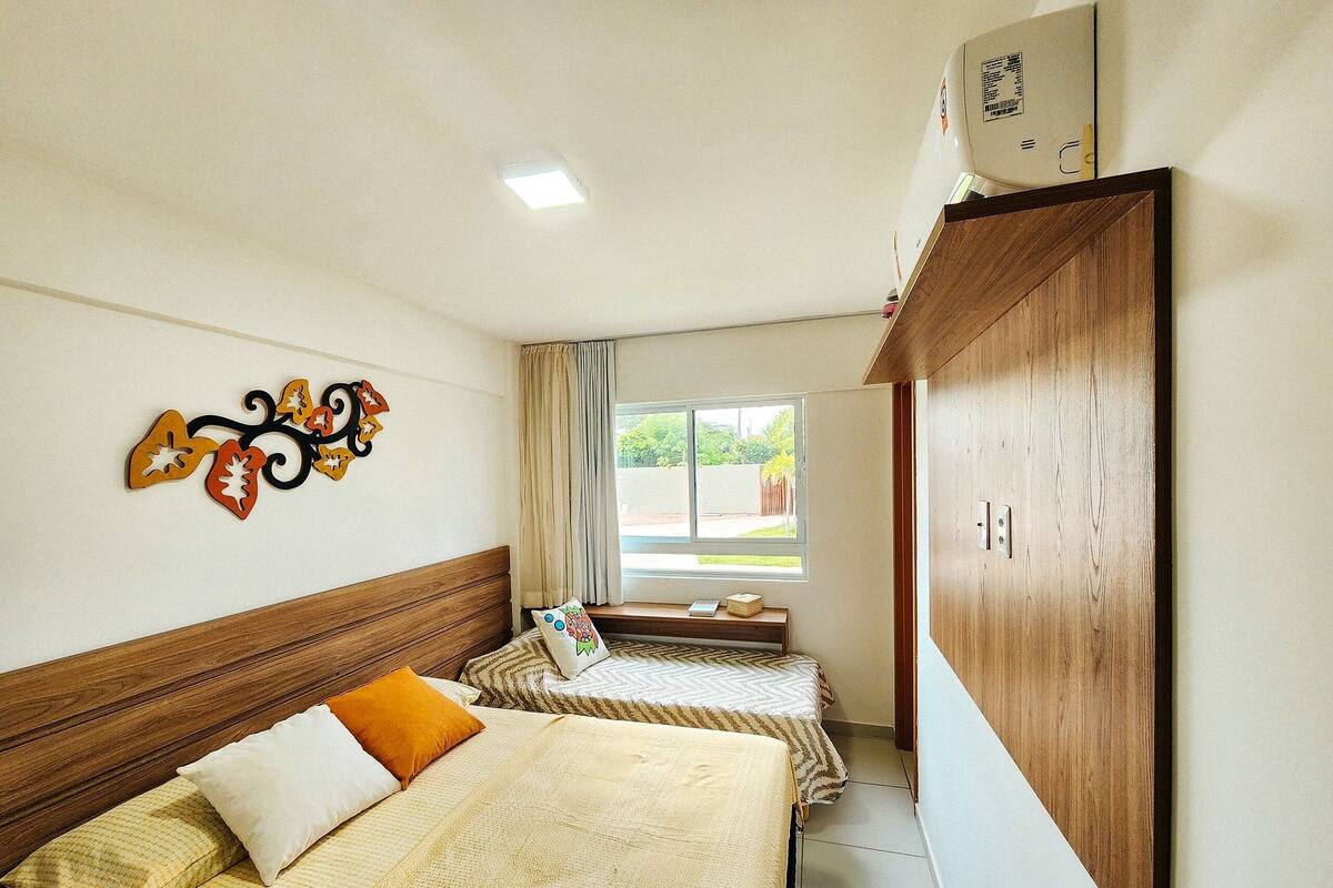 A hotel room with two beds, a wooden headboard, a decorative wall piece, a window with curtains, and a wardrobe.