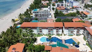 A resort with multiple buildings, a beach, and a pool area. - Lindos apartamentos no Porto Cayman (Tamandaré)