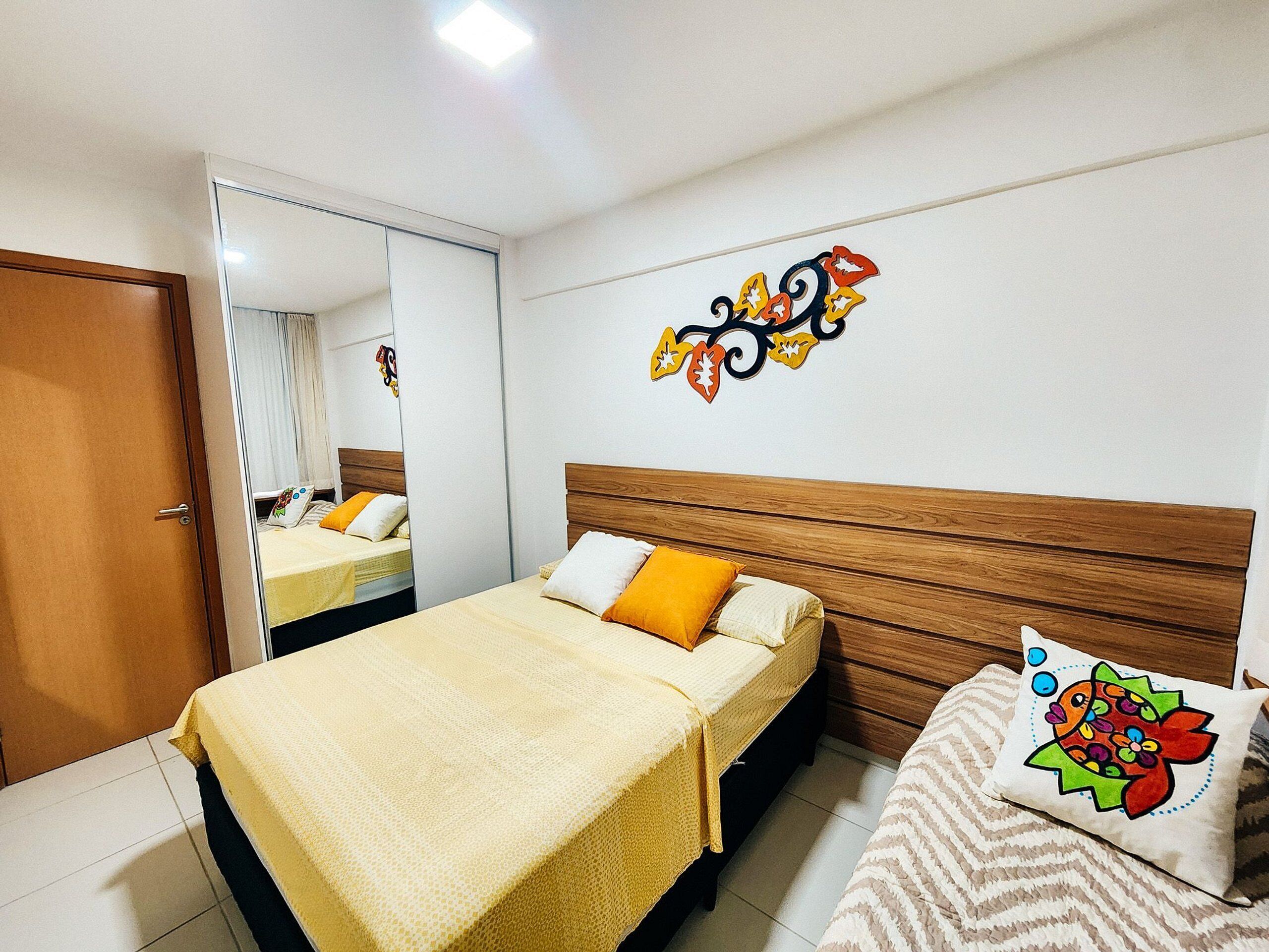 A bedroom with a bed, a nightstand, a mirror, and a wall decoration.