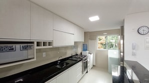 Una cocina moderna con armarios blancos, encimera negra, estufa a gas y refrigerador.