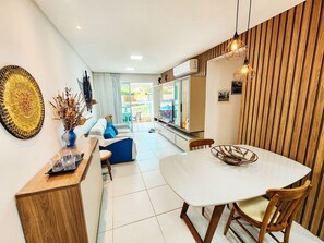 A modern kitchen with a dining area, featuring a white table, wooden chairs, and a kitchen island with a vase of dried flowers.
