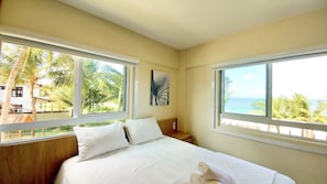 A bedroom with a bed, two windows, a nightstand, and a wall art piece. - Lindos apartamentos no Porto Cayman (Tamandaré)