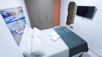 Una habitación de hotel con una cama, almohadas, una manta, un televisor y un cuadro de un atardecer sobre el océano.