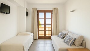 Een hotelkamer met twee eenpersoonsbedden, een bank, een houten tafel en een aan de muur bevestigde televisie.