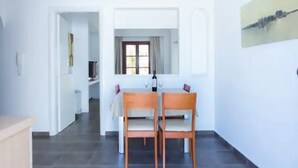 Een eethoek met een tafel en stoelen, een raam met gordijnen, en een schilderij aan de muur.