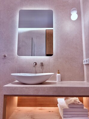 Une salle de bain avec un grand lavabo sur pied, un miroir, un porte-serviettes et une étagère en bois.