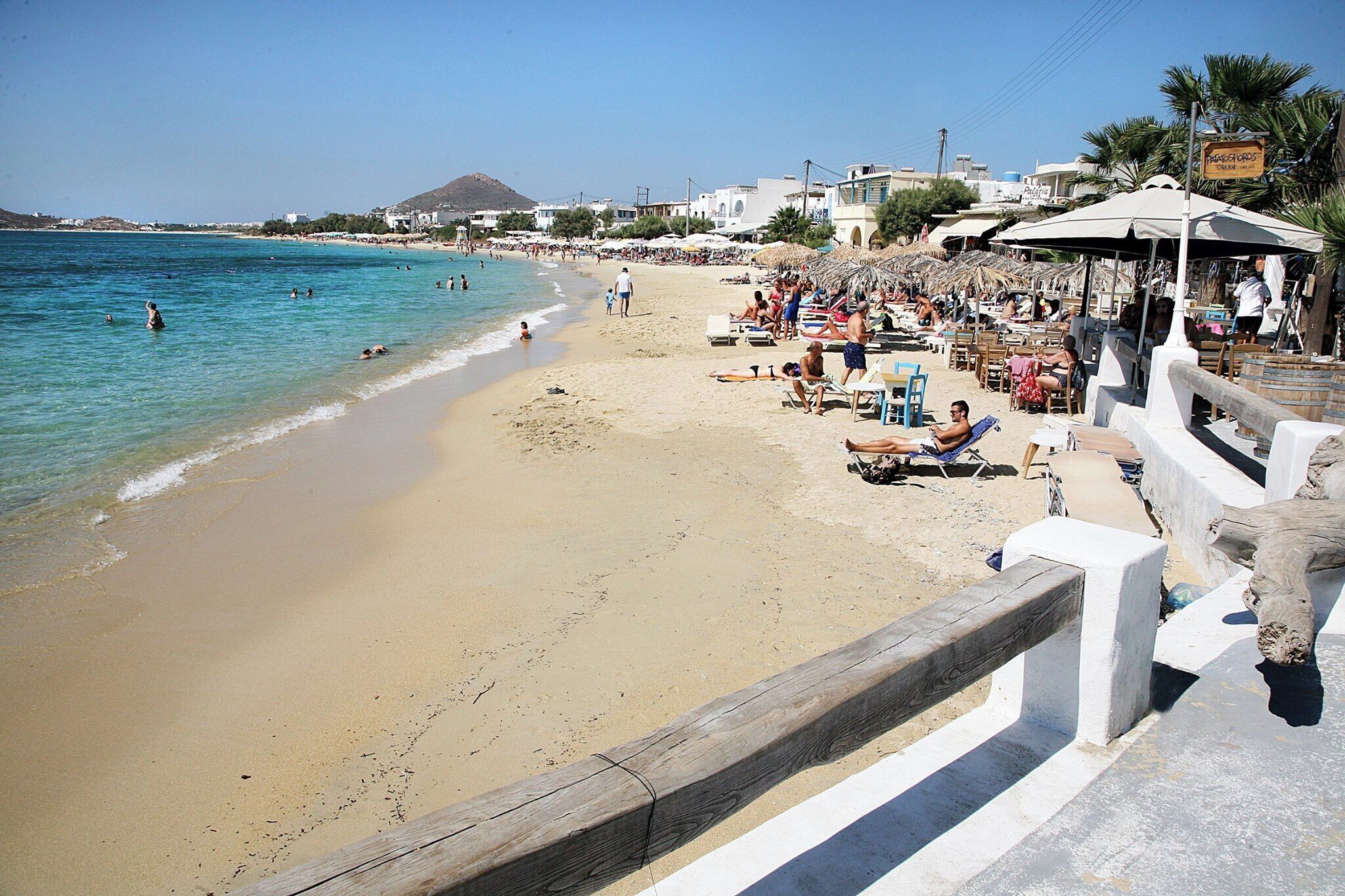 A beach with a wooden fence, beach chairs, umbrellas, and a signboard.