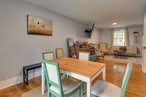 A dining area with a wooden table and chairs, a piano, a sofa, and a painting on the wall.