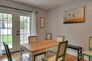 A dining area with a wooden table and green chairs, a sliding glass door, and a painting on the wall.