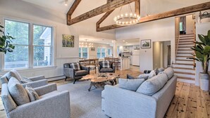 Un salon spacieux doté d’une grande fenêtre, d’un plafond en bois et d’un escalier menant à un autre niveau.