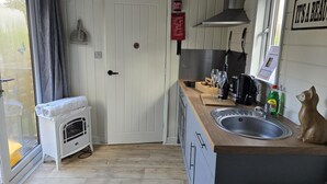 A compact kitchen with a wooden countertop, a sink, and a small oven. A fire extinguisher is mounted on the wall, and a sign reads "It's a beauty." - Glamping Hut - Sleeps 2, hot tub & Parking (Welshpool)
